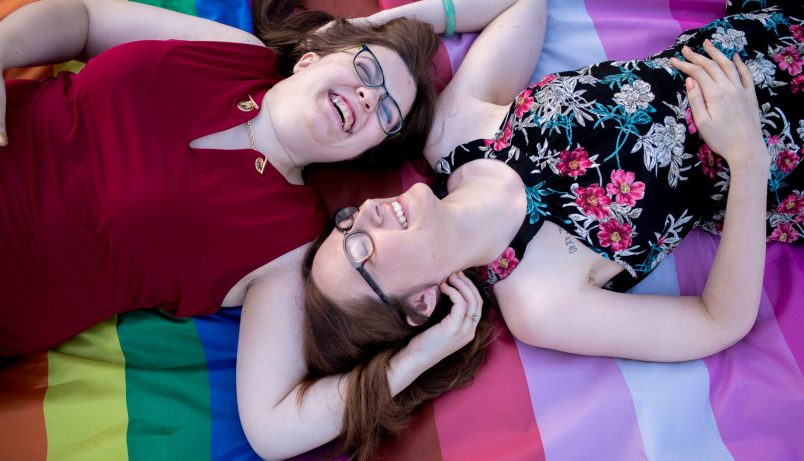 two women smiling and laying on a pride flag