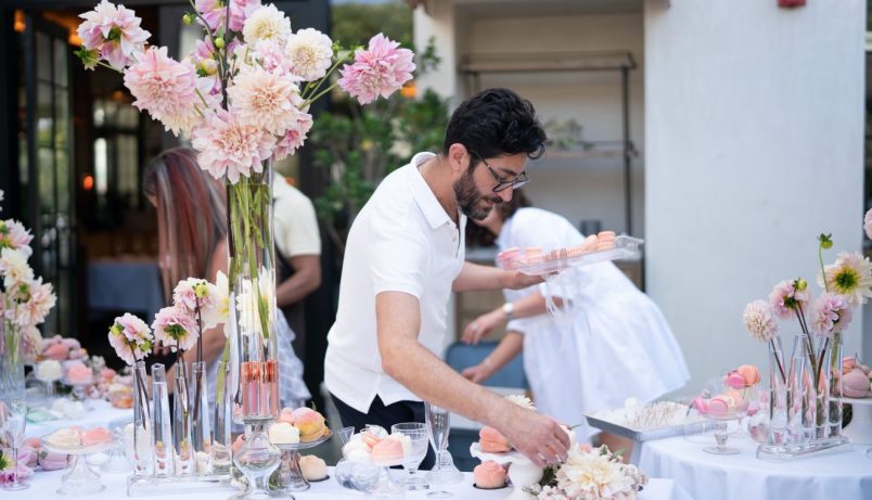 a man holding a tray of macaroons setting a table with flowers on it