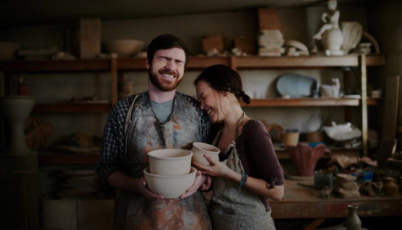 Warm toned portrait of carefree potters couple laughing in their small family shop