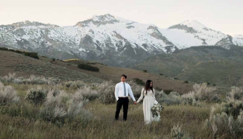 a bride and groom holding hands posing in front of a mountain